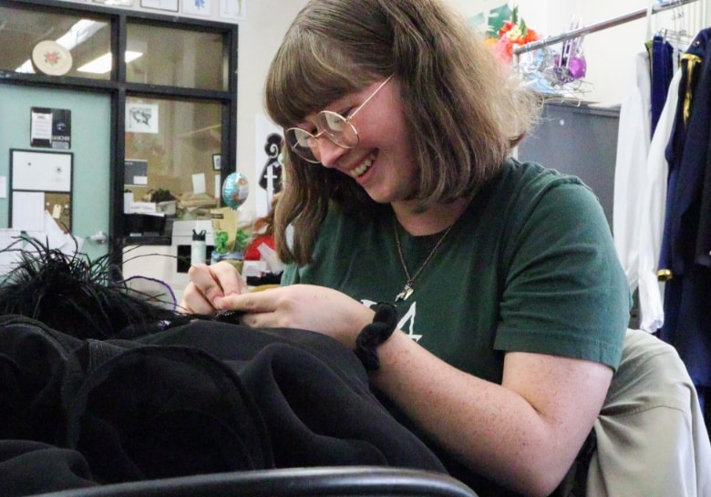 a student sewing on a coat in the costume shop
