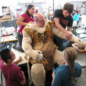 A group of costomers helping and actor into a costume